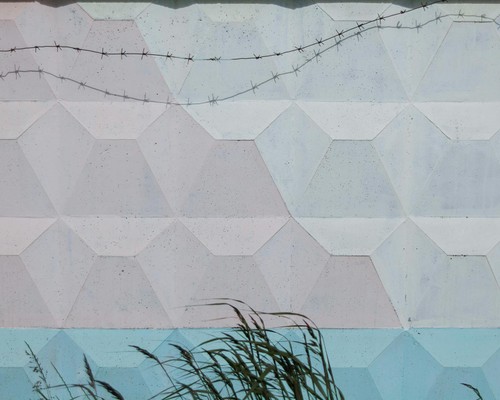 Textured pastel wall with geometric patterns and barbed wire adding contrast and intrigue.